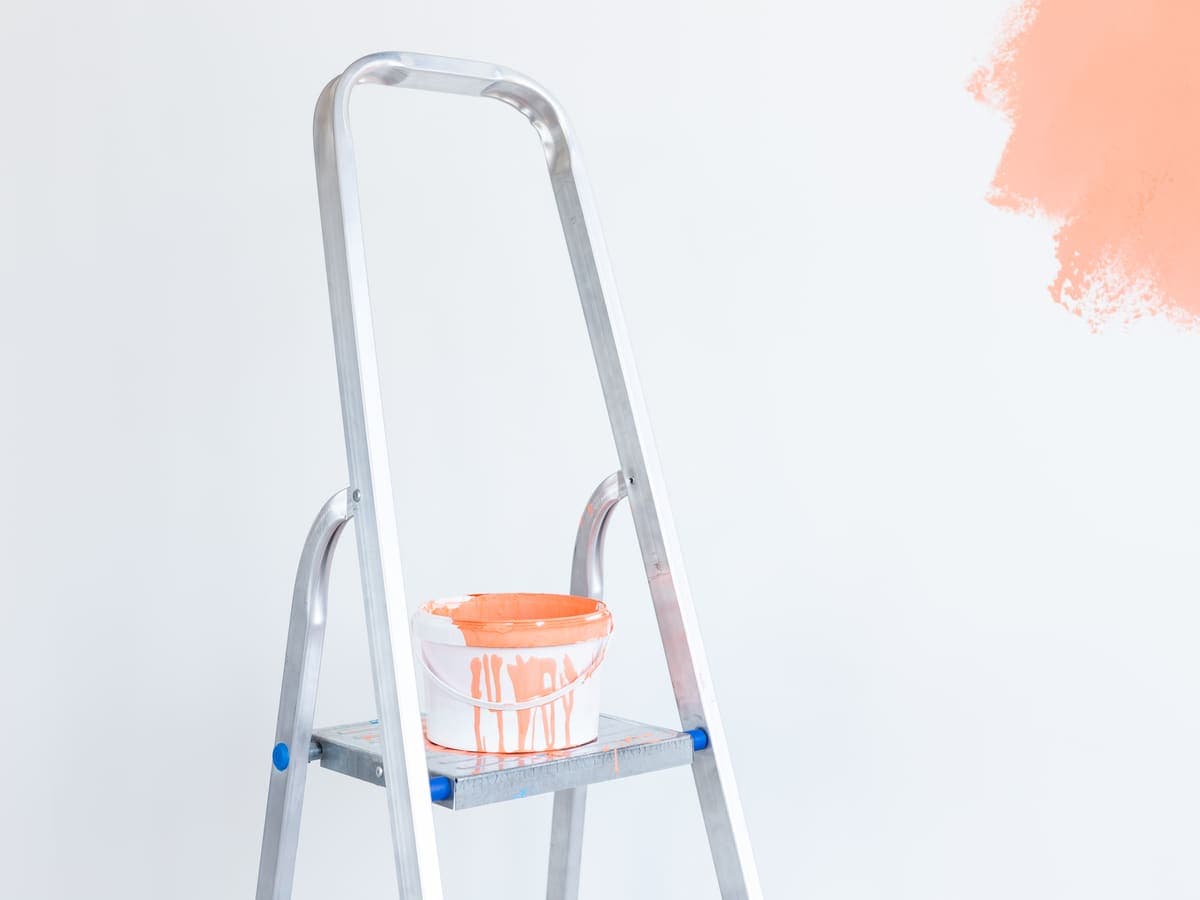 A ladder and paint supplies beside a freshly painted coral wall mid-renovation