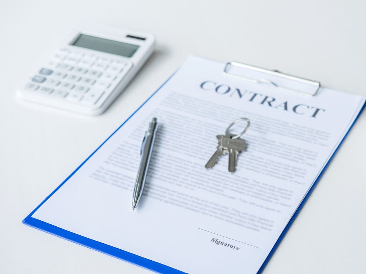 A purchase contract on a clipboard with house keys and a small model home