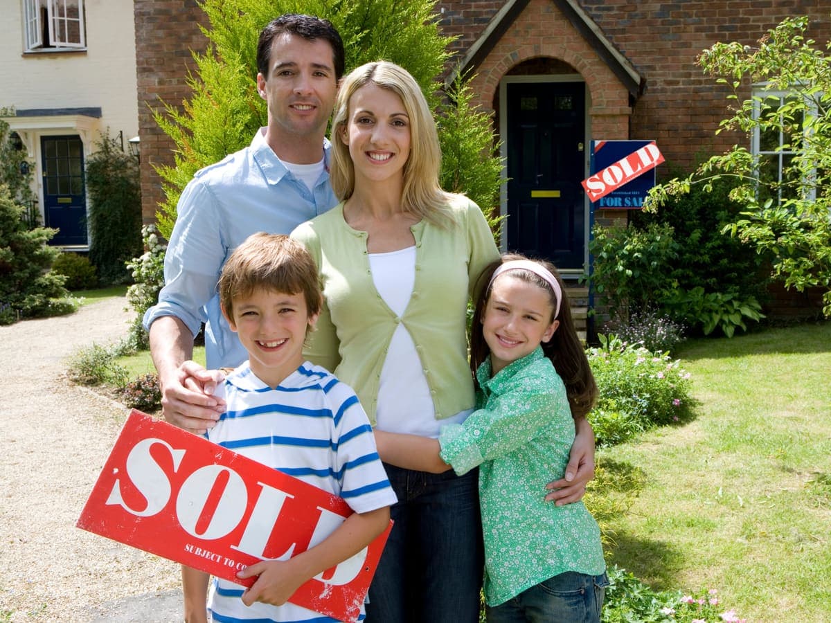 A young family standing in front of a home with a sold sign
