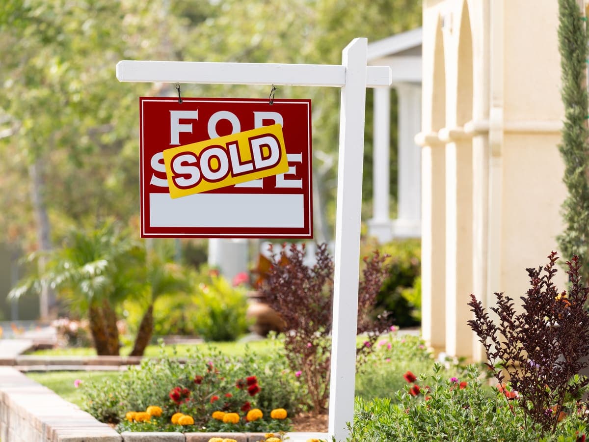 A for-sale sign with a sold banner in a sunny front yard