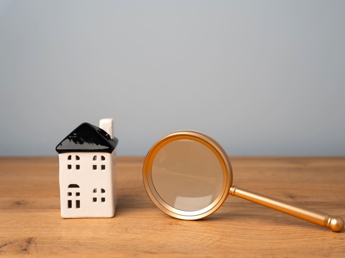 A small house figurine beside a magnifying glass on a wooden table