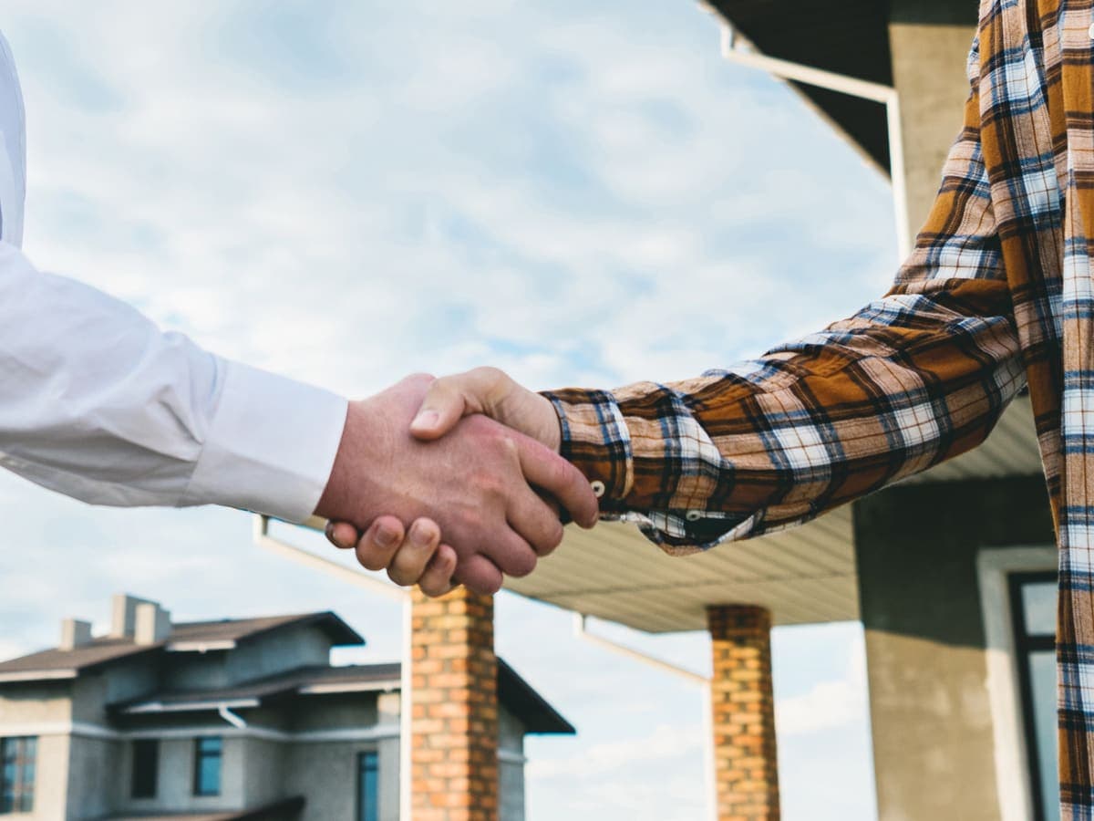 A buyer and seller shaking hands in front of a house