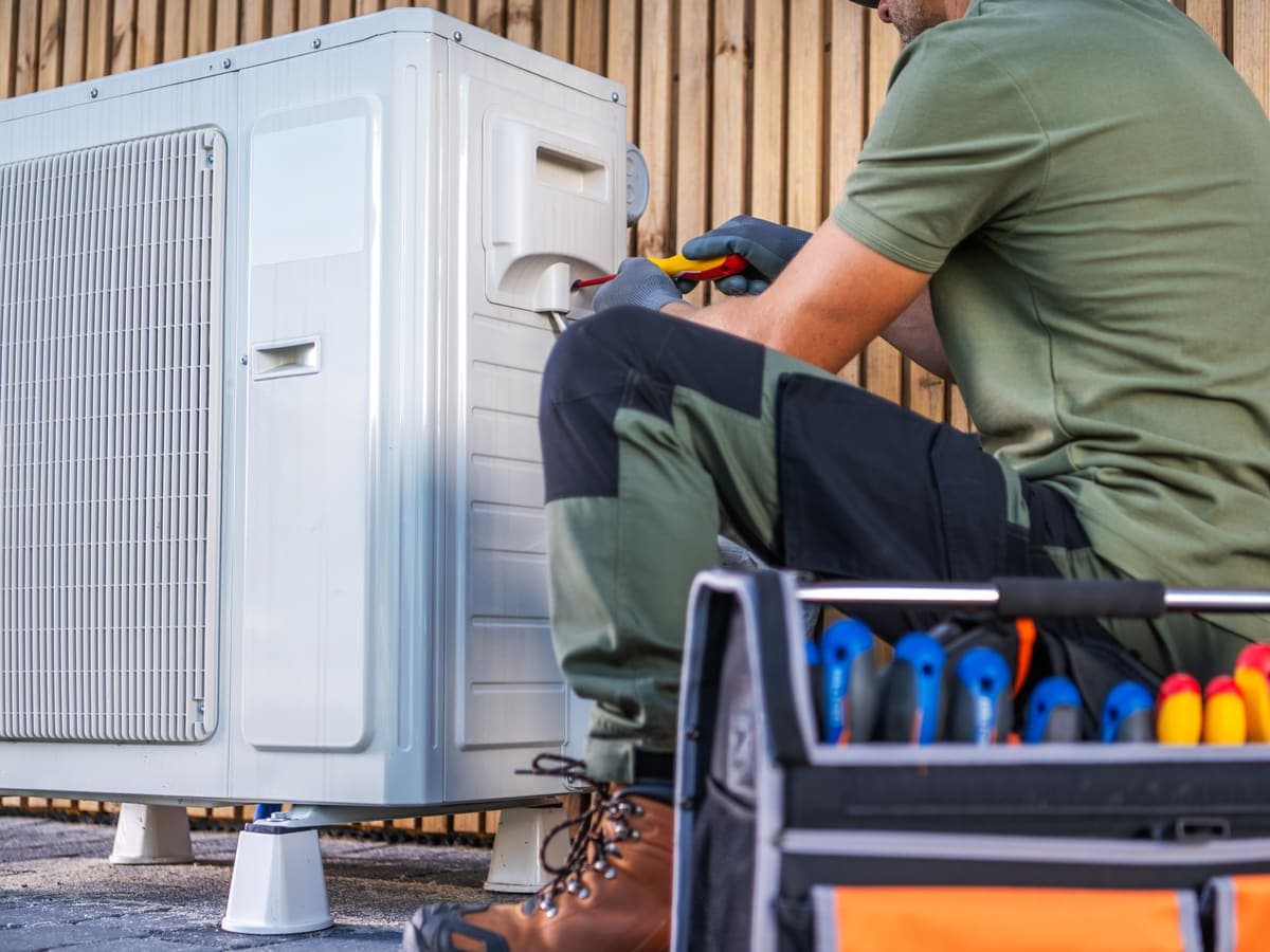 A technician servicing an outdoor air conditioning unit